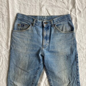 May include: A pair of light blue denim jeans with a faded look. The jeans have a classic five-pocket style and a button fly.
