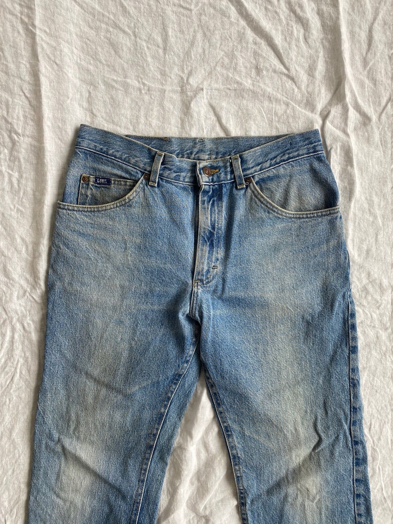 May include: A pair of light blue denim jeans with a faded look. The jeans have a classic five-pocket style and a button fly.