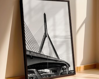 May include: A black and white framed wall art print featuring a low-angle perspective of a cable-stayed bridge with a prominent central pylon and diagonal support cables extending over a multi-level concrete highway structure under a bright sky.