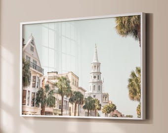 May include: A framed wall art print featuring a street scene with historic white buildings, a tall church steeple, and several palm trees under a clear sky. The architecture includes multi-story structures with balconies and windows.