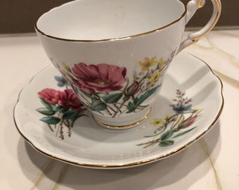 May include: A white teacup and saucer with a floral pattern. The cup has a gold rim and a delicate handle. The saucer has a matching floral pattern and a gold rim.