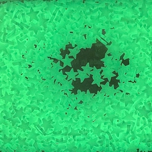 May include: A close-up image of a large quantity of green glow-in-the-dark stars. The stars are scattered randomly on a dark surface.