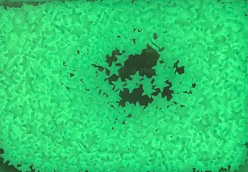 May include: A close-up image of a large quantity of green glow-in-the-dark stars. The stars are scattered randomly on a dark surface.