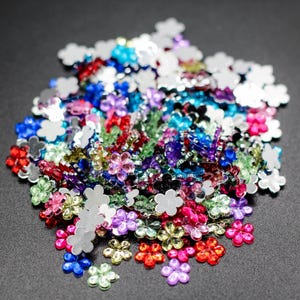 May include: A large pile of colorful flower-shaped rhinestones in various colors, including silver, red, blue, green, pink, and purple.