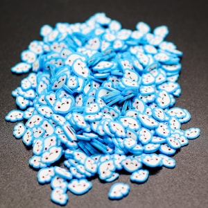 May include: A pile of blue and white cloud-shaped polymer clay slices. Each cloud has a smiling face with pink cheeks and black eyes. These small, decorative pieces are ideal for nail art or craft projects.