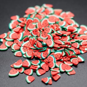 May include: A large pile of red and green watermelon-shaped sprinkles on a black background.
