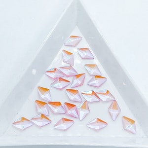 May include: A collection of iridescent pink and orange diamond-shaped rhinestones in a white triangular tray.