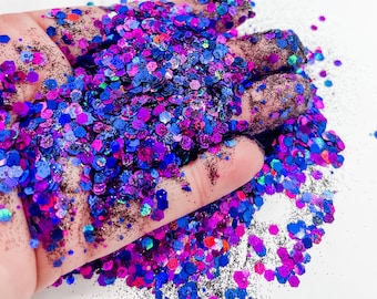 May include: A close-up of a hand holding a large amount of iridescent glitter. The glitter is a mix of blue, purple, pink, and black.