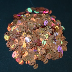 May include: A pile of iridescent brown, orange, yellow, green, purple, and pink football-shaped glitter.