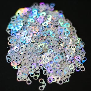 May include: A pile of iridescent silver glitter shaped like handcuffs. The glitter is scattered on a black background.