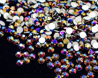 May include: A close-up of iridescent rainbow colored rhinestones scattered on a black surface. The rhinestones are various sizes and shapes.