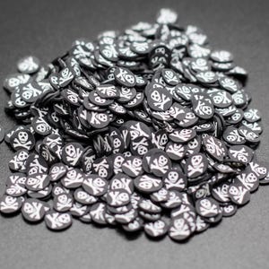 May include: A large pile of black and white skull and crossbones embellishments. The embellishments are small, round, and have a glossy finish.