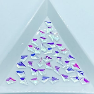 May include: A collection of iridescent, clear, diamond-shaped rhinestones on a white background.