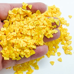 May include: A pile of yellow triangle-shaped confetti with orange polka dots. The confetti is made of polymer clay and is perfect for adding a fun and festive touch to crafts and projects.