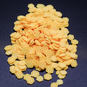 May include: A large pile of yellow flower-shaped sprinkles with a honeycomb pattern.