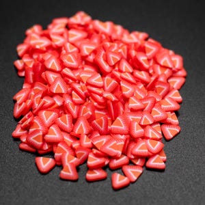 May include: A large pile of red and white triangle-shaped sprinkles, resembling strawberry slices, on a black background.