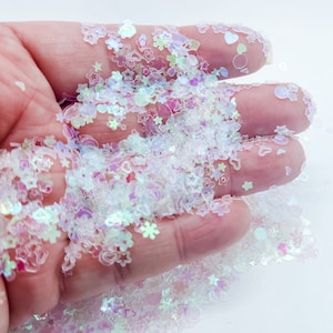 May include: A close-up of iridescent white glitter with various shapes, including stars, hearts, and snowflakes.