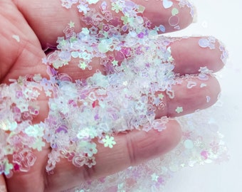 May include: A close-up of iridescent white glitter with various shapes, including stars, hearts, and snowflakes.