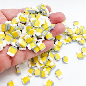 May include: A large pile of yellow and white beer mug shaped resin sprinkles. The sprinkles are in a hand, with some scattered on a white surface.