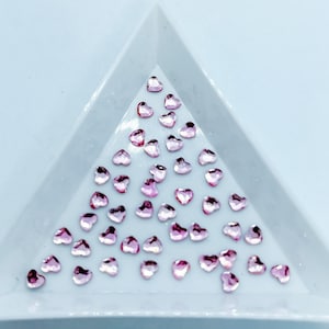 May include: A white triangular tray filled with pink heart-shaped rhinestones.