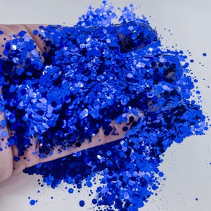 May include: A close-up of a hand holding a pile of bright blue glitter. The glitter is iridescent and has a holographic finish.
