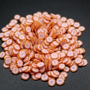 May include: A large pile of small, orange and white donut-shaped sprinkles. The sprinkles are made of polymer clay and have a glazed finish.