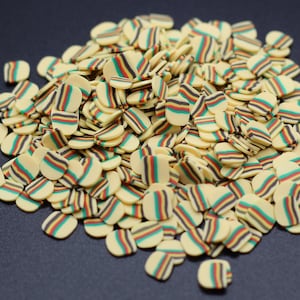 May include: A large pile of small, flat, oval-shaped confetti. The confetti is cream-colored with multi-colored stripes of red, green, black, and yellow.