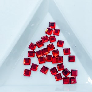 May include: A close-up of a white ceramic dish filled with red square-shaped rhinestones.