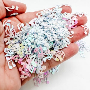 May include: A pile of iridescent white and pink musical note confetti. The confetti is in the shape of musical notes and is perfect for adding a touch of sparkle to crafts and projects.