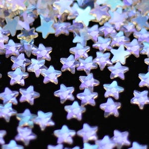 May include: A scattering of iridescent purple star-shaped rhinestones on a black background.