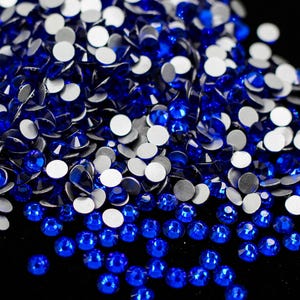 May include: A close-up of a pile of blue rhinestones and silver-backed rhinestones. The rhinestones are scattered on a black surface.