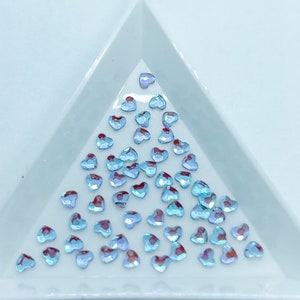 May include: A close-up of a light blue heart-shaped rhinestones scattered on a white surface.