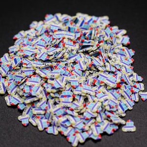 May include: A large pile of colorful, small, heart-shaped sprinkles with a blue, white, and red design. The sprinkles are made of polymer clay and are perfect for decorating cakes, cupcakes, and other desserts.