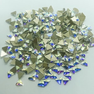 May include: A pile of iridescent, triangular rhinestones with a metallic silver backing. The rhinestones have a multifaceted design that reflects light, creating a rainbow effect. These decorative embellishments are ideal for crafts and jewelry making.