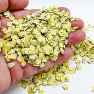 May include: A large pile of yellow and white square sprinkles with a beer mug design. The sprinkles are in a hand, and some are scattered on a white surface.