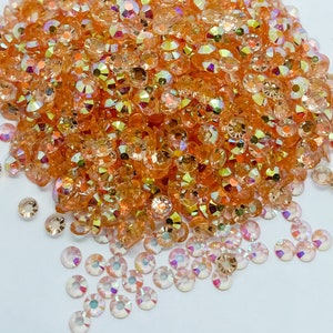 May include: A large pile of iridescent orange rhinestones, with a smaller pile of clear rhinestones in the foreground.