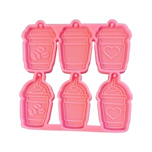 May include: Pink silicone mold with six cavities shaped like coffee cups. Each cup has a different design, including coffee beans and a heart.