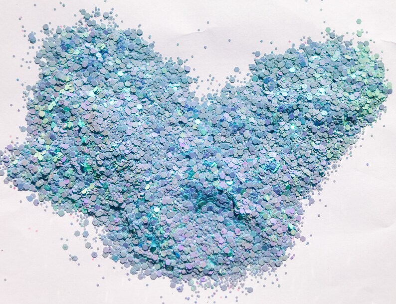 May include: A close-up of iridescent blue glitter, scattered on a white surface. The glitter is in the shape of a heart.