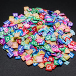May include: A large pile of colorful plastic letter tiles. The tiles are in various colors, including red, blue, green, yellow, orange, and pink. The letters are white and are in uppercase.