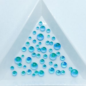 May include: A white triangular tray with a scattering of iridescent blue and green glass beads.