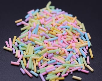 May include: A pile of pastel colored sprinkles in the shape of long, thin cylinders. The sprinkles are a mix of pink, blue, yellow, and green.