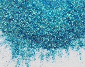 Peut inclure: Gros plan sur une pile de paillettes chatoyantes de couleur turquoise. Les paillettes sont denses, avec une texture scintillante. Le fond est une surface blanche et propre, créant un contraste qui met en valeur l'éclat des paillettes. Idéal pour les loisirs créatifs et les cosmétiques.