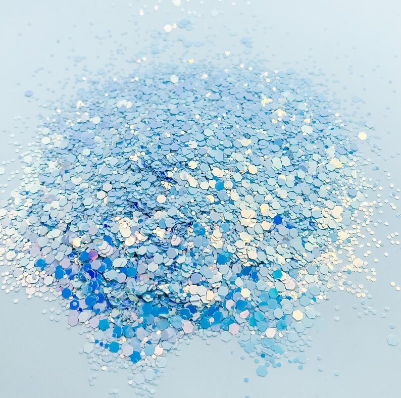 Puede incluir: Un mont&oacute;n de purpurina azul iridiscente sobre un fondo azul claro. La purpurina est&aacute; compuesta por peque&ntilde;as piezas hexagonales.