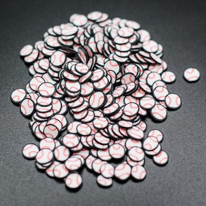 May include: A large pile of white and red baseball-themed sprinkles with black outlines. The sprinkles are scattered on a black surface.
