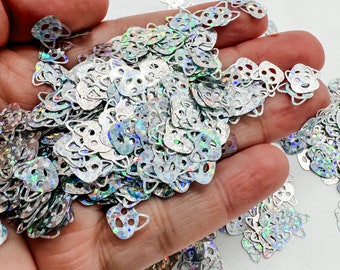 May include: A pile of silver iridescent glitter in the shape of cat faces. The glitter is scattered on a hand.