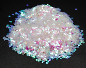 Puede incluir: Un montón de purpurina iridiscente en forma de estrella en tonos blancos, rosas y azules. La purpurina tiene una calidad brillante y reflectante, que atrapa la luz y crea un efecto brillante. Ideal para manualidades y decoraciones.