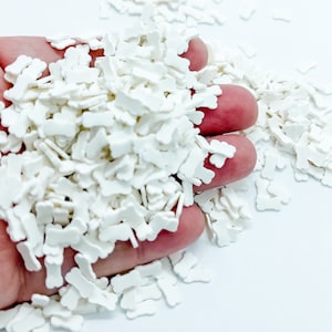 May include: A large pile of white bone-shaped sprinkles. The sprinkles are small and have a slightly raised texture.