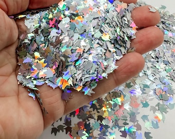 May include: A pile of iridescent holographic unicorn-shaped glitter in various sizes. The glitter is silver with a rainbow sheen.