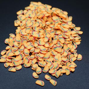 May include: A large pile of yellow, orange, and green taco-shaped sprinkles. The sprinkles are made of a soft, pliable material and are perfect for decorating cakes, cupcakes, and other desserts.