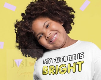 May include: A young person wearing a white t-shirt with the text "MY FUTURE IS BRIGHT" in yellow letters. The person is smiling and wearing a black tulle skirt.